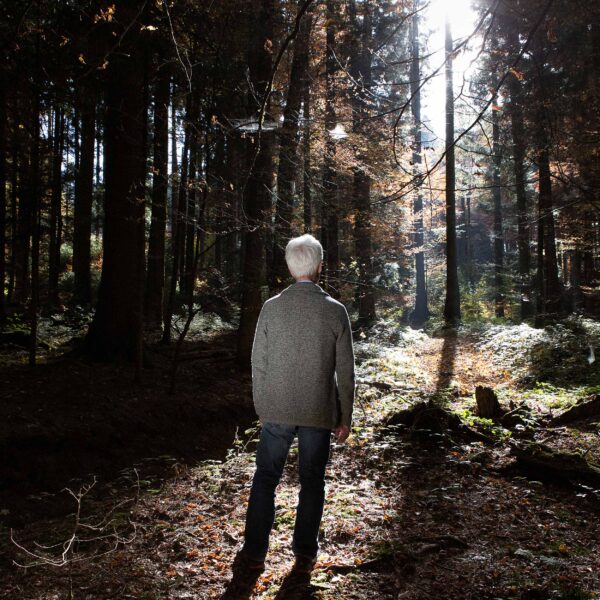 Mann steht im Wald und schaut in die Sonne