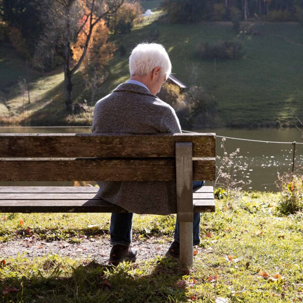 Älterer Herr sitzt nachdenklich auf einer Bank am Weiher
