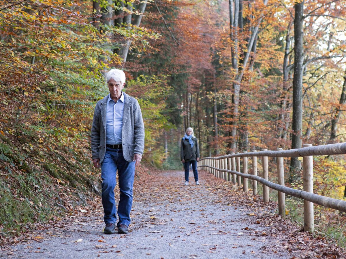 Mann spaziert traurig und nachdenklich im Wald, seine Frau ist stehen geblieben