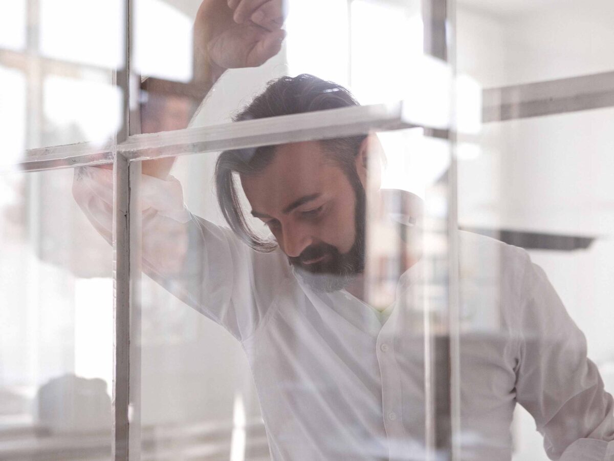 Mann stützt sich mit dem Arm am Fenster ab und denkt nach