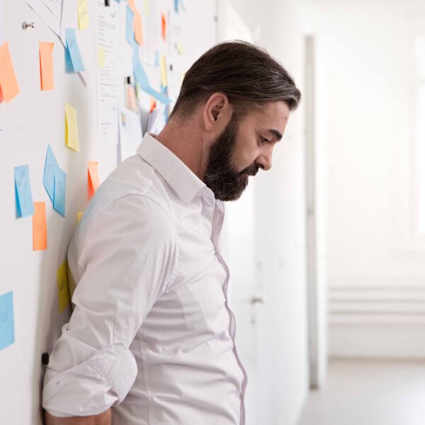 Mann lehnt nachdenklich an einer Wand mit Notizzetteln