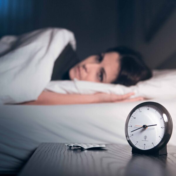 Frau liegt schlaflos im Bett, auf dem Nachttisch liegen Tabletten